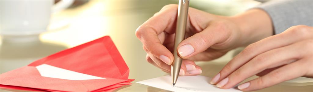 Close up of a woman hand writing a greeting card while sittin at a desk at home.