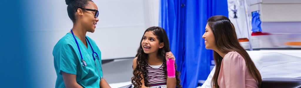 A girl sits on a bed holding up her wrist with a  cast.