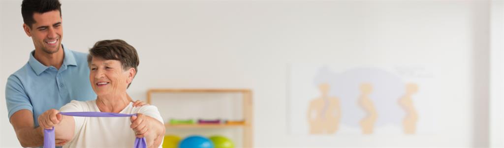 Smiling physiotherapist helping older woman while exercising with resistance tape.