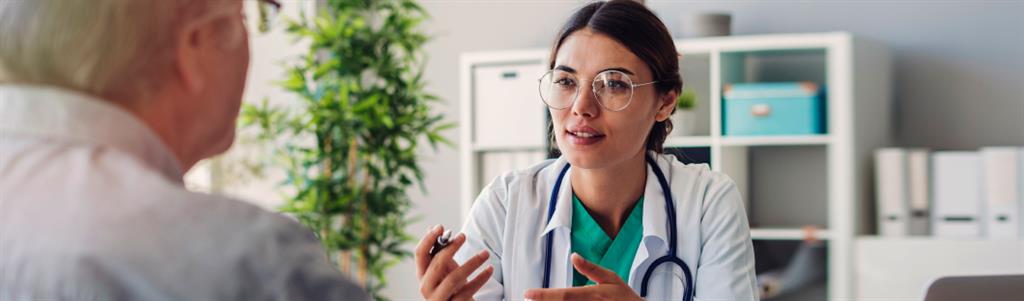 A doctor and a patient sit across a desk from one another having a discussion.